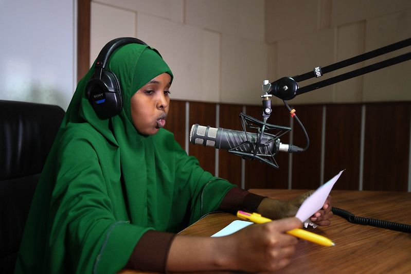 Young woman in a hijab with headphones on speaking into a microphone